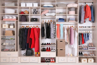 Guardaroba moderno color legno chiaro con abbigliamento femminile assortito, incluse borse di lusso e scarpe col tacco esposte sui ripiani.